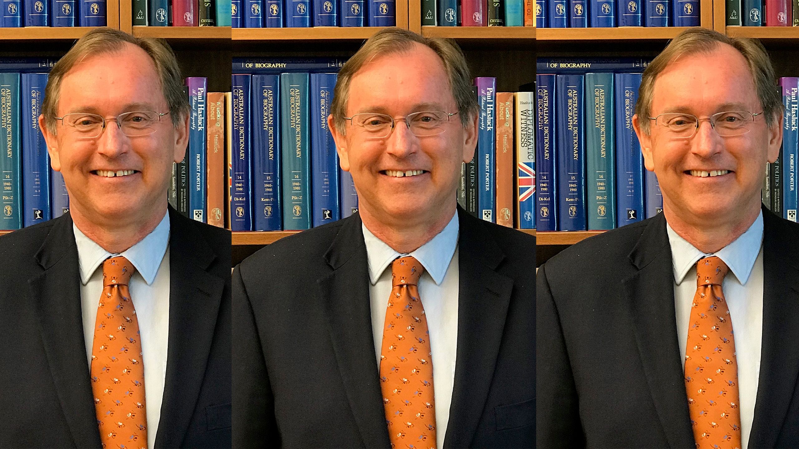 Professor Don Markwell wearing an orange tie and standing in front of a bookcase