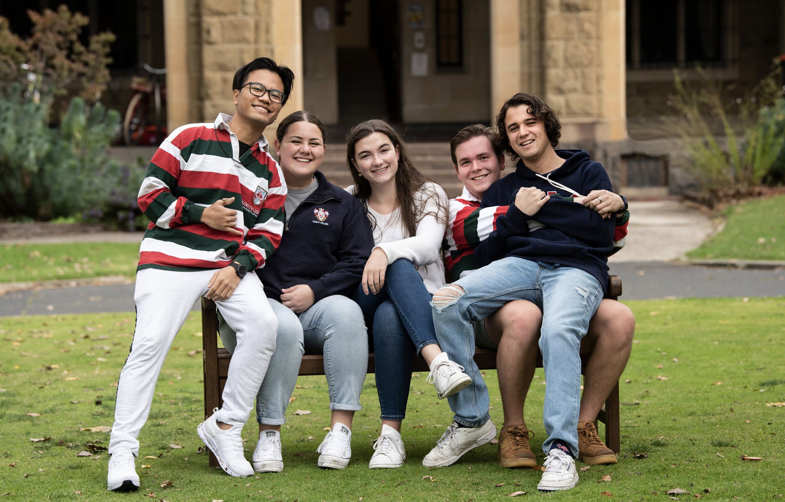 Trinity students, some wearing college candystripes, gather on a bench for a group photograph, 2021.