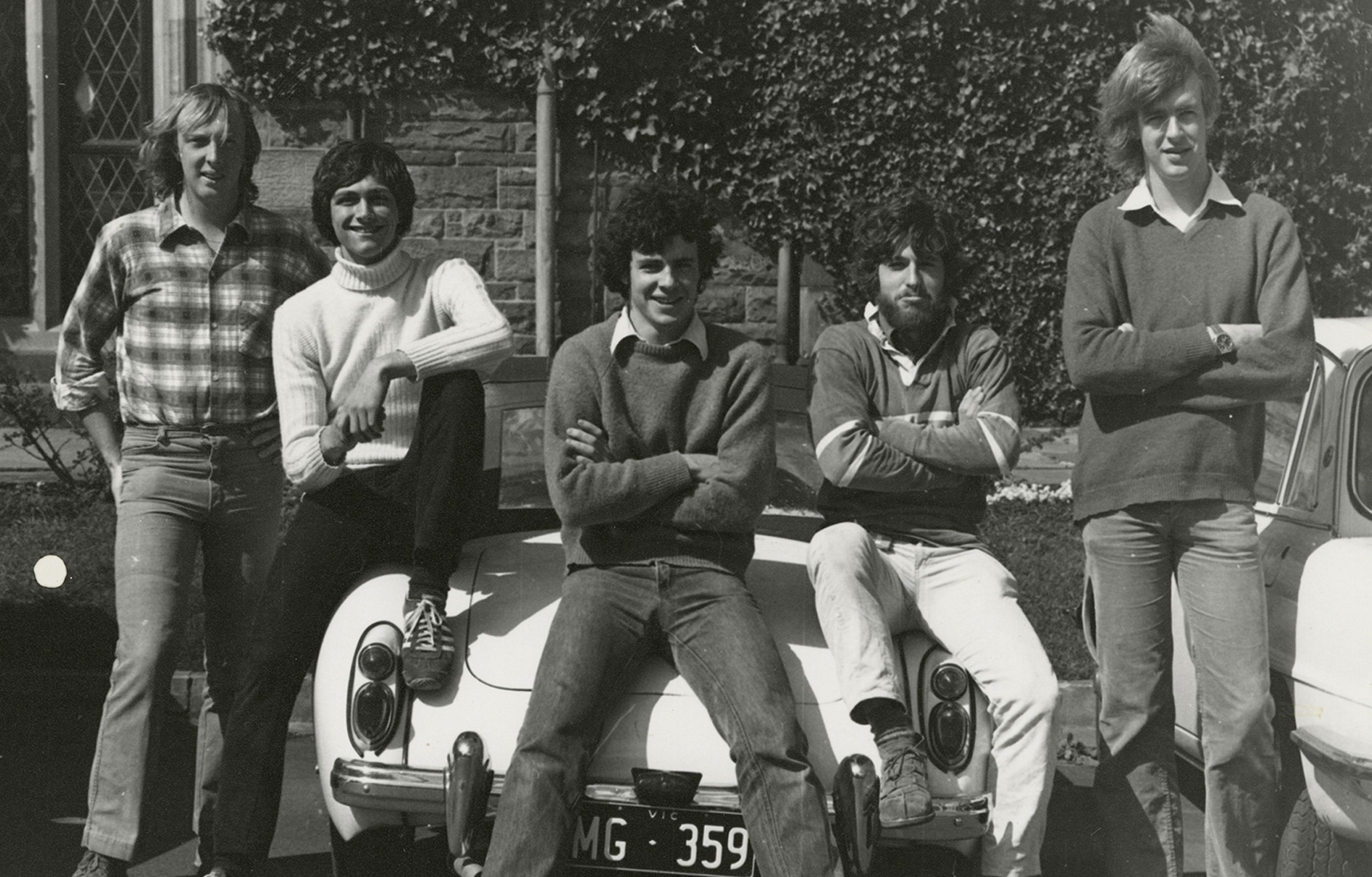 Male students gather around, and some seated, on the boot of a car at Trinity College, mid-1970s.