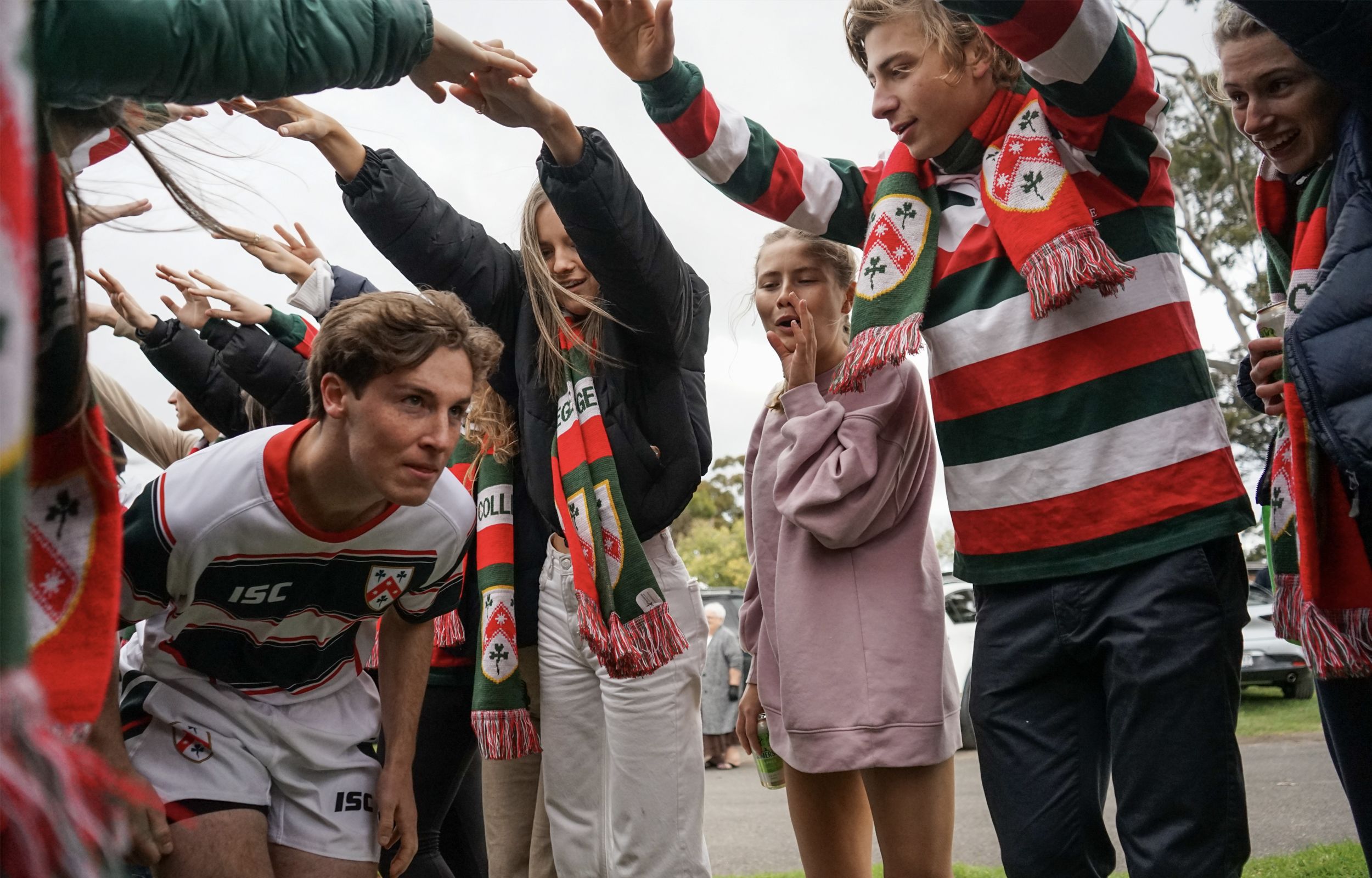 Jack Reddrop (TC 2021) crouches to pass through a tunnel of supporter's arms before the victorious men's rugby match against Ormond in 2021.